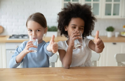 Smiling multiethnic sisters kids drink clean pure mineral water show thumbs u